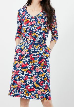 Bloemenjurk met een marineblauwe achtergrond, met rode, roze, gele en witte bloemen. V-hals, driekwart mouwen en zijzakken.