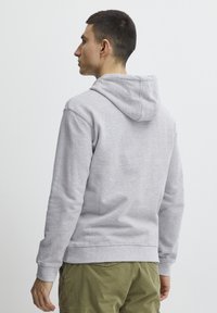 Šedá mikina s kapucí na šňůrku, měkká textura, žebrované manžety a lem. Zadní pohled ukazuje jednoduchý design bez log a vzorů.