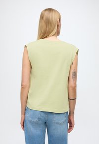 Haut vert clair sans manches avec une coupe décontractée, un col rond et des accents aux épaules, accompagné d'un jean en denim bleu clair.