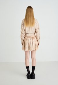 Light brown checkered oversized shirt with puffed sleeves, paired with a beige pleated skirt and black platform shoes. Black thigh-high socks.