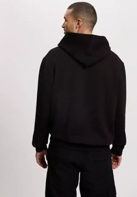 Czarny sweter z kapturem z dużym kapturem, ribbowanymi mankietami i dołem oraz luzem. Miękka tkanina o minimalistycznym wzornictwie.