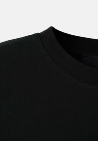 Crna pamučna majica s okruglim izrezom, glatke teksture i suptilnim detaljima šavova oko ovratnika. Jednostavan, minimalistički dizajn.