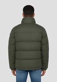 Giacca a vento imbottita verde oliva con collo alto, caratterizzata da un design trapuntato e finitura testurizzata, indossata sopra jeans blu. Vista posteriore.