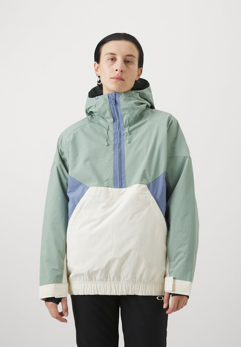 Veste légère à capuche ; présente des couleurs menthe, bleu et crème, une taille élastique et une fermeture éclair sur le devant.