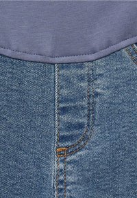 Tela de mezclilla azul con una costura visible y un leve desvanecimiento. Tela de sudadera gris en la parte superior con un cuello de canalé y costuras.