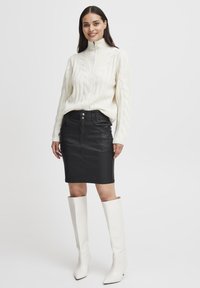 Pulover alb tricotat cu model de cablu, guler înalt, fustă creion din piele neagră și cizme albe cu bot ascuțit până la genunchi. Textură netedă și design ajustat.