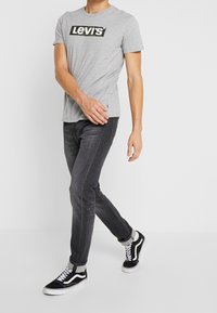 Camiseta de algodón gris con el logo negro de "Levi's", combinada con jeans gris oscuro y zapatillas Vans negras. Ajuste simple y casual con los puños arremangados.
