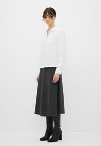Blusa bianca con zip frontale, maniche lunghe; abbinata a una lunga gonna grigia con righe verticali e stivali neri col tacco al ginocchio.