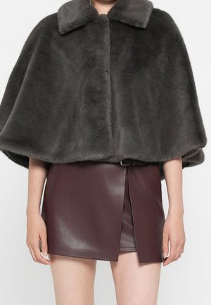 Personne portant une cape en fausse fourrure gris foncé avec un large col sur une mini-jupe en cuir bordeaux avec une fente devant et une ceinture.