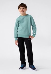 Svetlo turkizna majica z okroglim izrezom, črne športne hlače in mornarsko modri čevlji z turkiznimi poudarki. Mehka tkanina z detajli logotipa na obeh kosih oblačil.