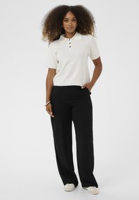Kremowa koszulka polo z krótkim rękawem, płaskim kołnierzykiem i zapięciem na trzy guziki, połączona z czarnymi spodniami o szerokiej nogawce i wysokim stanie.