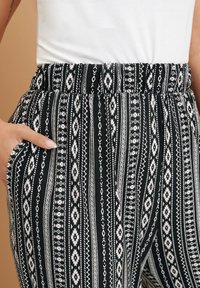 Pantalones de patrón blanco y negro con una cinturilla elástica, que cuentan con rayas verticales y un bolsillo en el costado. Textura de tela suave.
