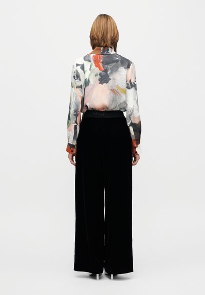 Bluza ușoară cu imprimeu floral, cu mâneci lungi și nasturi la manșete, asortată cu pantaloni din catifea negri, cu talie înaltă și croială largă.