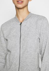 Grijze bomberjack van een gestructureerde stof, met ritssluiting aan de voorkant en geribde kraag. Heeft zijzakken en een aansluitend model.