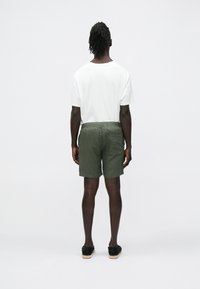 Conjunto masculino com uma t-shirt branca de manga curta, calções verdes com um bolso traseiro e calçado preto com sola texturizada.