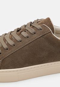 Brune semskede sneakers med flade taupe snørebånd, beige gummisål og subtile syninger. Glat tekstur med rund tådesign.