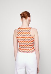 Top bez rukávů s mnohobarevným zig-zag vzorem v oranžové, růžové a zlaté barvě. Vyroben z texturované látky, je dobře padnoucí a módní.