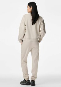 Beżowy komplet bluza i spodnie z miękkiego materiału, o luźnym kroju, z prążkowanymi mankietami i paskiem ściągającym w talii, zestawiony z czarnymi butami sportowymi.