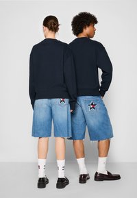 Marineblå sweat-shirt parret med lyseblå denim shorts med en stjernepatch, flagrende kant og hvide strømper med striber. Sorte sko fuldender outfittet.