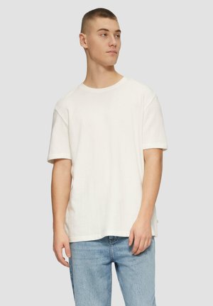 Weißes Kurzarm-T-Shirt aus strukturiertem Baumwollstoff, mit Rundhalsausschnitt und lockerer Passform, kombiniert mit hellblauen Jeans.