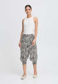 Top bianco senza maniche abbinato a pantaloni harem larghi a scacchi bianchi e neri, con polsini arricciati e una texture di tessuto liscia.