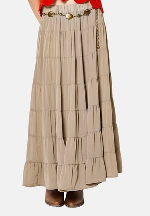 Falda larga beige de capas con cinturilla elástica, combinada con botas marrones de cuero hasta el tobillo y un cinturón decorativo de cadena dorada.