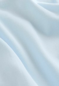 Lyseblåt stof med en blød, tekstureret overflade, der viser blide folder og bølger og fremhæver dens glatte, vævede struktur.