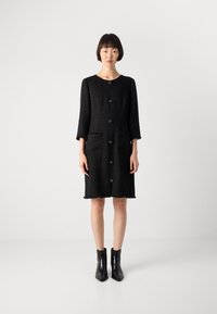 Abito in tweed nero con scollatura rotonda, maniche a tre quarti, due tasche frontali e bottoni dorati sul davanti. Finitura testurizzata.