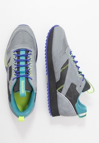 Šedé tenisky z kombinace síťoviny a semiše, s modrými a zelenými akcenty a texturovanou podrážkou. Mají kontrastní tkaničky a značku na jazyku.