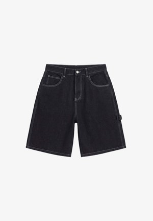 Jonge man draagt een rood bloemenkorte mouwen overhemd over een wit grafisch t-shirt, zwarte lange shorts, witte sneakers en witte sokken met logo's.