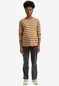 Langarm-T-Shirt in Braun mit Streifen aus Baumwolle, kombiniert mit dunklen Jeans und cremefarbenen Sneakers; hat einen lässigen Schnitt und einen Rundhalsausschnitt.