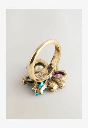 Arany színű gyűrű sima, vékony sávval, amely egy virágos alapon helyezkedik el, különböző formájú kék, rózsaszín és átlátszó kristály díszekkel.