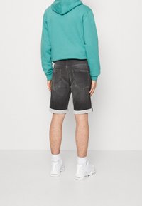 Shorts de denim negro con puños remangados, bolsillos traseros y una textura suave, combinados con una sudadera color teal y zapatillas blancas.