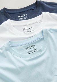 Drei gefaltete T-Shirts mit Rundhalsausschnitt in Marineblau, Weiß und Hellblau, jeweils mit dem Markenlabel „NEXT musée“ im Kragen.