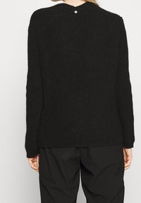 Schwarzer gestrickter Pullover mit strukturiertem Muster, langen Ärmeln und einem Knopfdetail am Rücken. Einfaches Design mit lockerer Passform.