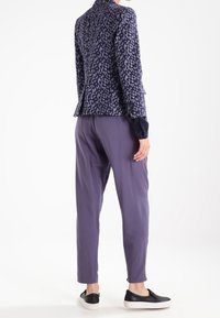 Navy modrý blazer se vzorem a přiléhavým střihem, kombinovaný se světle fialovými kalhotami a černými botami na slip. Hladká textura látky.