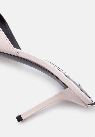 Κοντινό πλάνο ενός μπεζ γυναικείου παπουτσιού με ψηλό τακούνι, που δείχνει ένα λεπτό τακούνι στιλέτο και ραμμένο δερμάτινο πάνω μέρος σε λευκό φόντο.