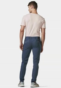 Himmelbluse mit kurzen Ärmeln in Hellrosa und dunkelblauen, taillierten Hosen, die mit Knopf- und Taschendetails versehen sind, kombiniert mit grau-weißen Turnschuhen.