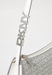 Gray DKNY handbag with white leather accents, featuring a silver logo on the strap, zip closure, and a textured pattern on the body.