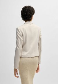 Beige blazer met een op maat gemaakte snit, enkele knoopsluiting, met een vesperrand en decoratieve stiksels op de mouwen, gecombineerd met een geribbelde rok.