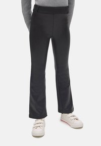 Leggings negras de campana hechas de un tejido suave y elástico con una cinturilla ancha. Combinados con zapatillas blancas que tienen un sutil acento rojo.