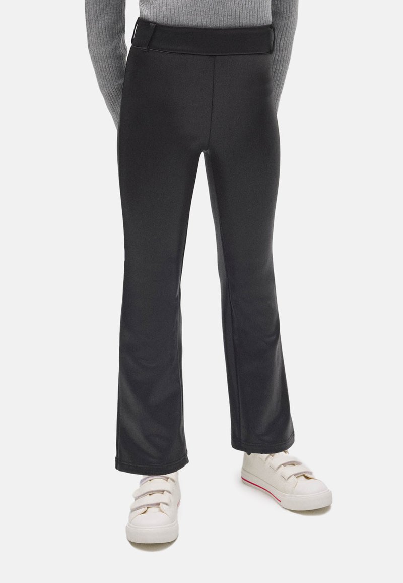 Leggings negras de campana hechas de un tejido suave y elástico con una cinturilla ancha. Combinados con zapatillas blancas que tienen un sutil acento rojo.