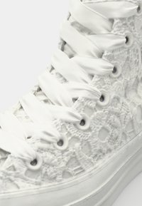 Texturált anyagból készült fehér magasszárú sneaker, csipkebonddal, fényes fehér fűzővel és fém szemfogakkal.
