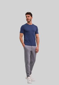T-shirt blu navy a maniche corte abbinato a pantaloni della tuta grigi chiari. I pantaloni hanno una vestibilità affusolata e tasche laterali. Calzature sono delle sneakers bianche.