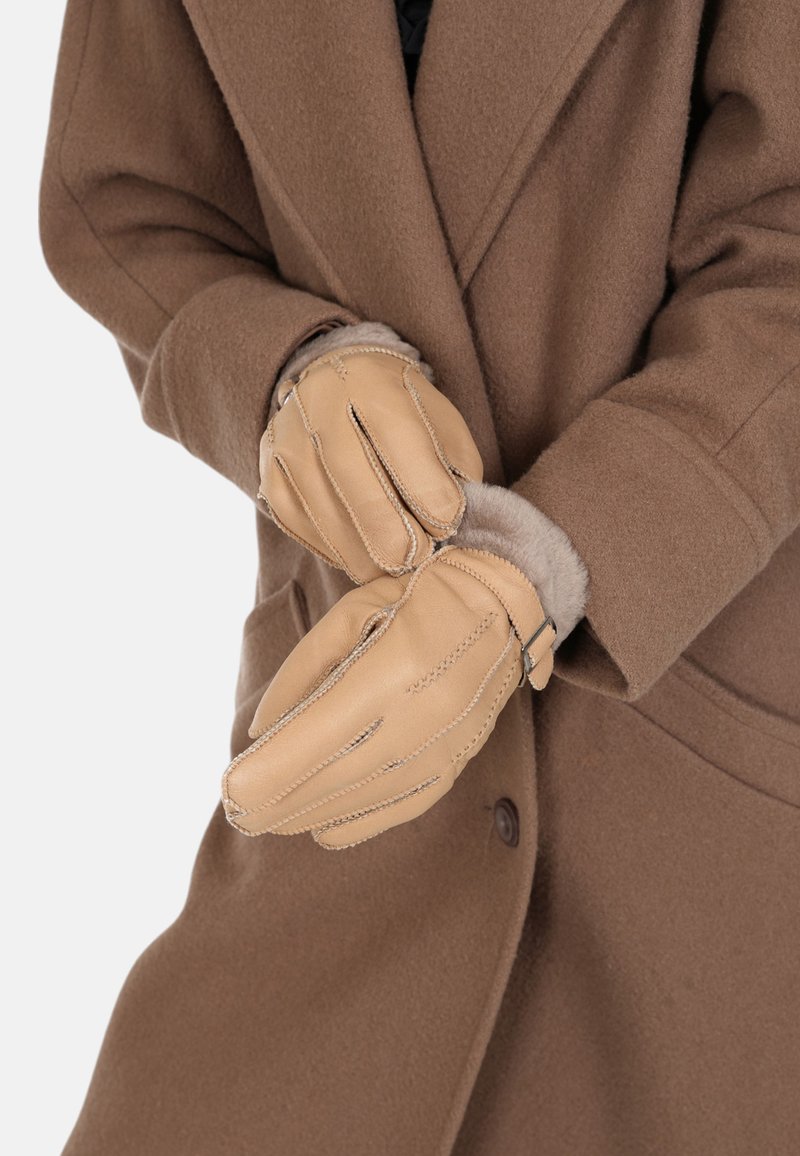 Tan leather gloves with fur lining, featuring a cinched wrist and decorative stitching, worn over a brown coat.