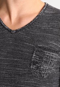 Czarny i szary sweter na szydełku z dekoltem w serek, wykonany z teksturowanej tkaniny, z kieszonką w kratę na lewej piersi.