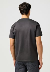 Camiseta gris de manga corta con cuello redondo, hecha de algodón suave. Presenta un diseño liso con una textura suave, combinada con jeans oscuros.
