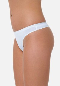 String blanc en matière douce avec une bande élastique lisse. Le design offre une couverture minimale avec une silhouette épurée et une texture douce.