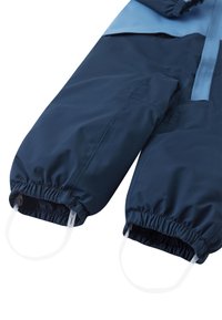 Námornícky modrý nepremokavý zimný overal s elastickými manžetami a svetlomodrými akcentmi. Má hladký povrch a praktické očká na zápästiach.