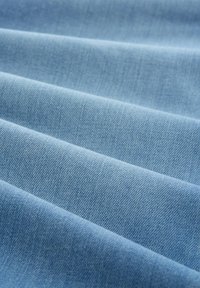 Tejido de denim azul claro con superficie texturada y doblada, que muestra un acabado suave y un sutil patrón de tejido.